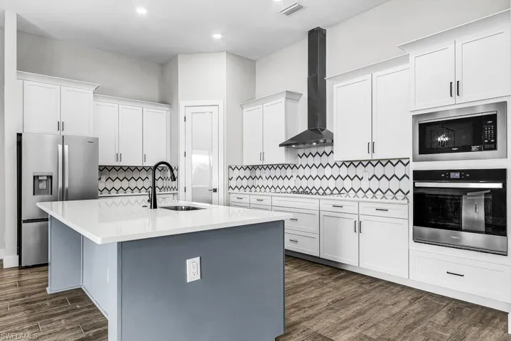 Kitchen featuring appliances with stainless steel finishes, wall chimney range hood, white cabinets, and gray cabinetry
