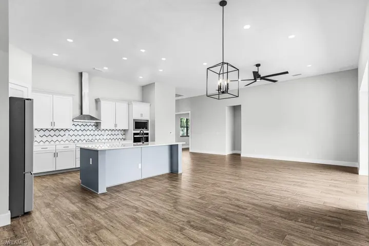 Kitchen featuring white cabinets, open floor plan, a center island with sink, stainless steel appliances, and decorative light fixtures