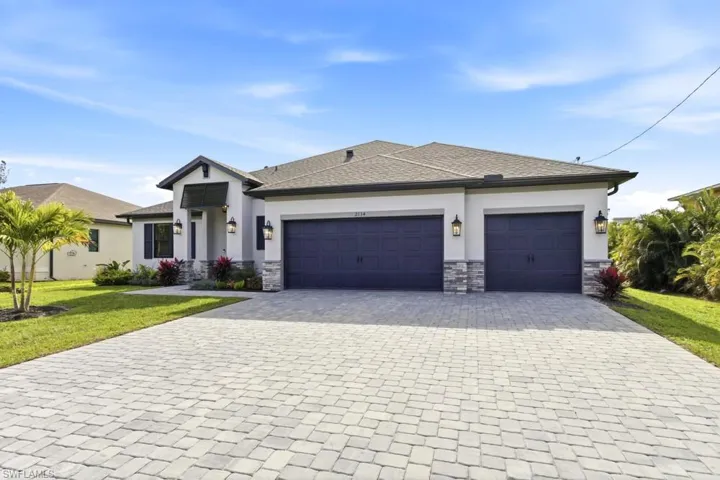 View of front facade with a garage, decorative driveway, stone siding, and a front yard