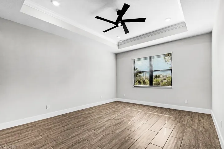 Unfurnished bedroom with wood finished floors, ornamental molding, a tray ceiling, and a ceiling fan