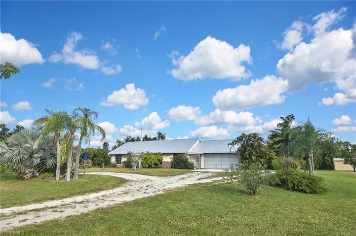 View of front of property featuring dirt driveway, a front lawn, and an attached garage
