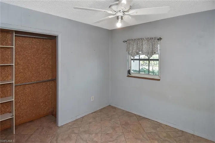 Unfurnished bedroom featuring a closet, a textured ceiling, a ceiling fan, and light tile patterned floors