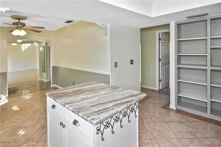 Kitchen with light tile patterned floors, white cabinets, light countertops, a ceiling fan, and a center island