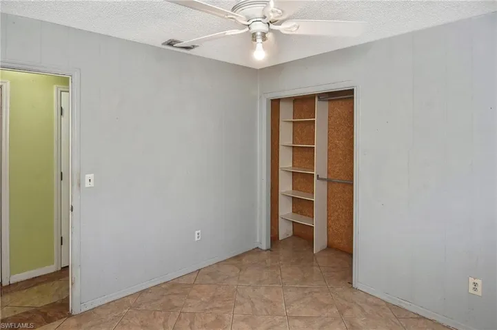 Unfurnished bedroom with a textured ceiling, ceiling fan, wood walls, a closet, and light tile patterned flooring