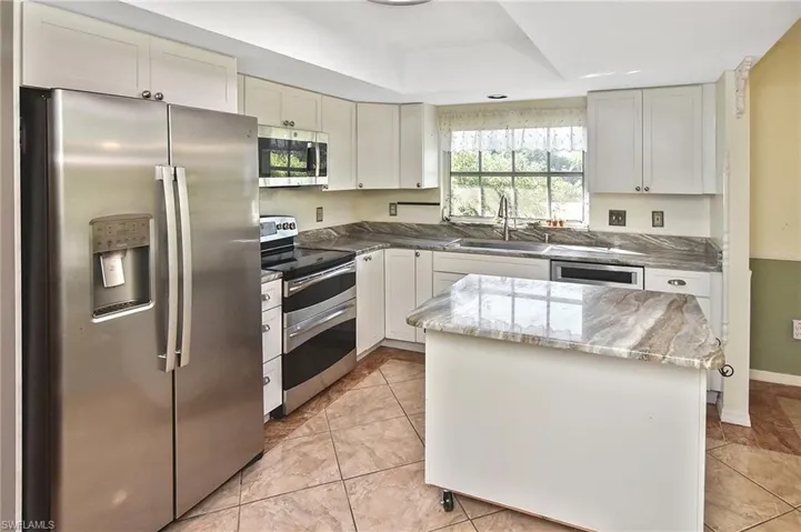 Kitchen with appliances with stainless steel finishes, a center island, light tile patterned floors, and white cabinetry