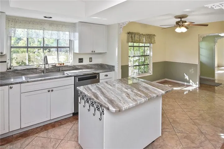 Kitchen with white cabinetry, stainless steel dishwasher, light tile patterned flooring, ceiling fan, and a kitchen island