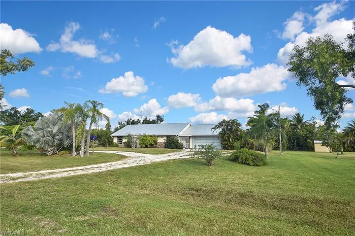 View of front of house with a front lawn, dirt driveway, and an attached garage