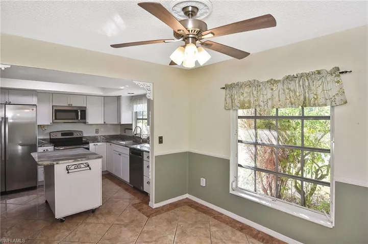 Kitchen featuring stainless steel appliances, a center island, a textured ceiling, light tile patterned floors, and a ceiling fan