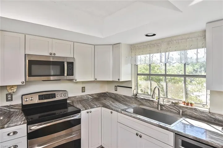 Kitchen with stainless steel appliances, white cabinets, and dark stone countertops