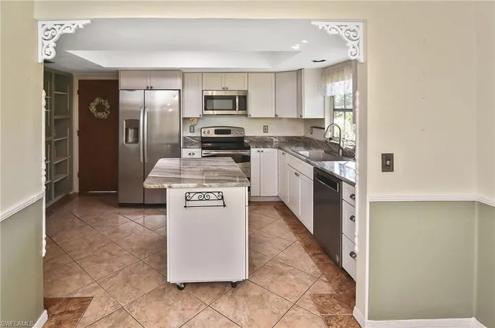 Kitchen with appliances with stainless steel finishes, dark stone counters, a center island, and light tile patterned floors