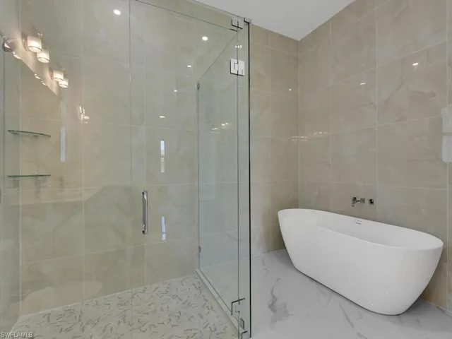 Bathroom featuring shower with separate bathtub and tile walls