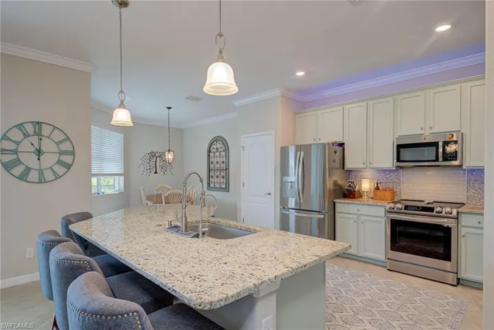 Kitchen featuring appliances with stainless steel finishes, decorative backsplash, light tile patterned floors, crown molding, and hanging light fixtures