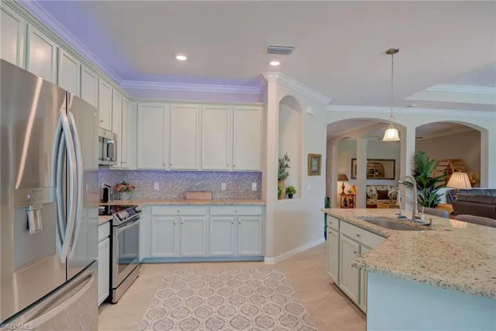 Kitchen with stainless steel appliances, crown molding, decorative light fixtures, tasteful backsplash, and light stone countertops