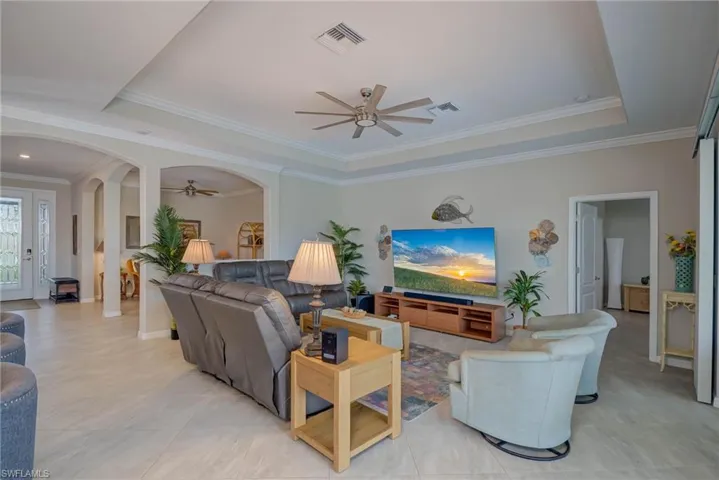Living room with a tray ceiling, a ceiling fan, crown molding, arched walkways, and light tile patterned floors