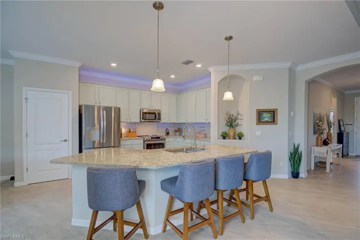 Kitchen featuring stainless steel appliances, a kitchen bar, tasteful backsplash, ornamental molding, and arched walkways