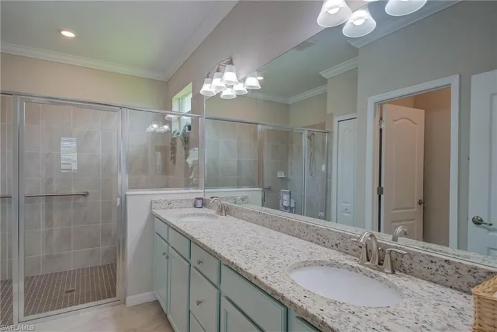 Bathroom with a shower stall, double vanity, crown molding, and light tile patterned floors