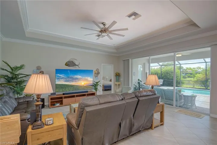 Tiled living area with a tray ceiling, a sunroom, ornamental molding, and ceiling fan