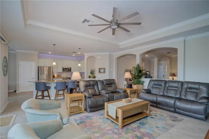 Living room with a raised ceiling, crown molding, light tile patterned floors, arched walkways, and a ceiling fan