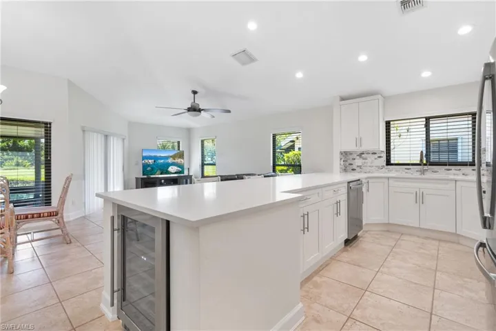 Kitchen with kitchen peninsula, backsplash, wine cooler, ceiling fan, and light tile floors