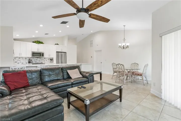 Tiled living room featuring high vaulted ceiling and ceiling fan with notable chandelier