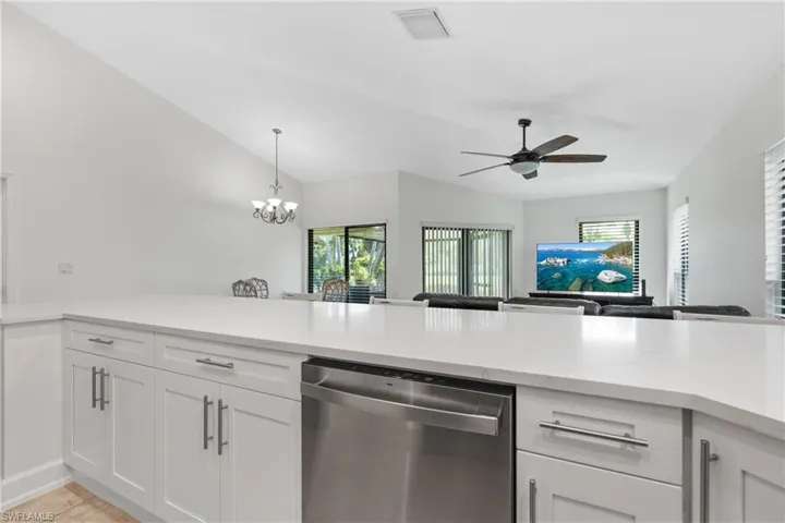 Kitchen featuring a healthy amount of sunlight, lofted ceiling, stainless steel dishwasher, and ceiling fan with notable chandelier