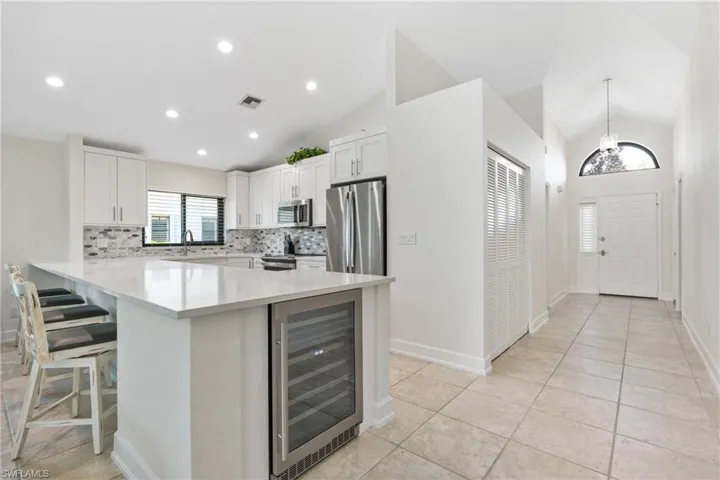 Kitchen featuring white cabinetry, appliances with stainless steel finishes, backsplash, wine cooler, and pendant lighting