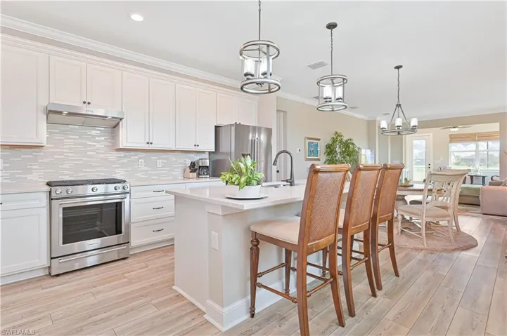 Kitchen with stainless steel appliances, under cabinet range hood, a sink, a chandelier, and crown molding