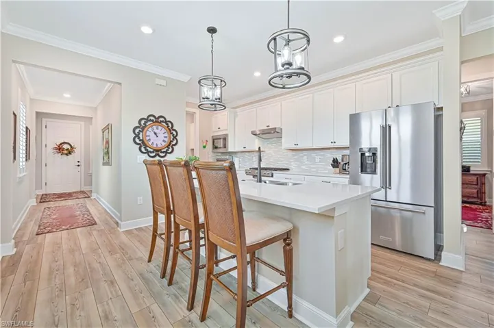 Kitchen with stainless steel appliances, a breakfast bar area, under cabinet range hood, light countertops, and white cabinetry