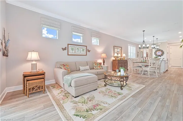 Living room with light wood finished floors, ornamental molding, baseboards, a chandelier, and recessed lighting