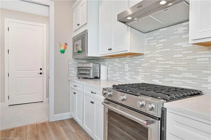 Kitchen with stainless steel appliances, exhaust hood, light wood finished floors, white cabinetry, and baseboards