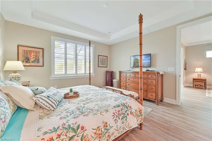 Bedroom featuring a tray ceiling, crown molding, light wood-style flooring, and baseboards
