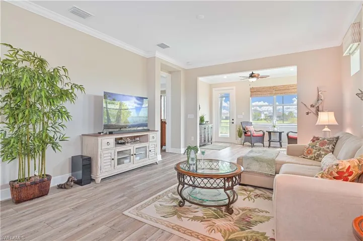 Living room with light wood-style floors, a ceiling fan, crown molding, and baseboards