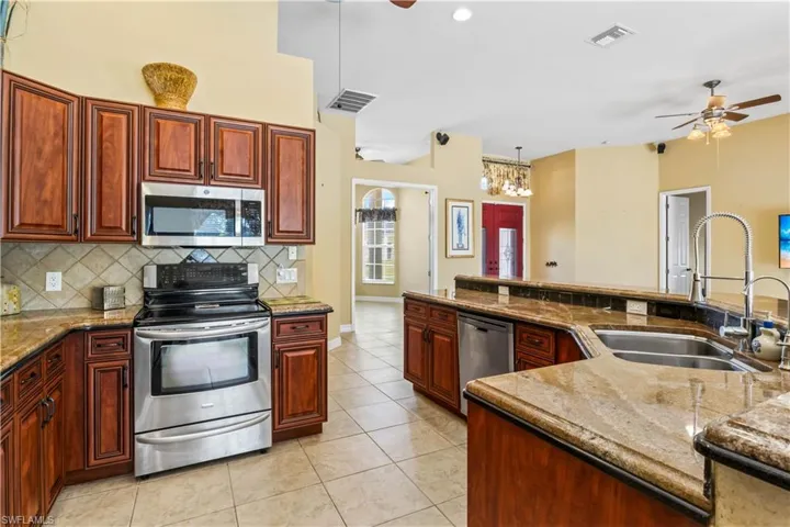 Kitchen with sink, hanging light fixtures, ceiling fan, stainless steel appliances, and decorative backsplash