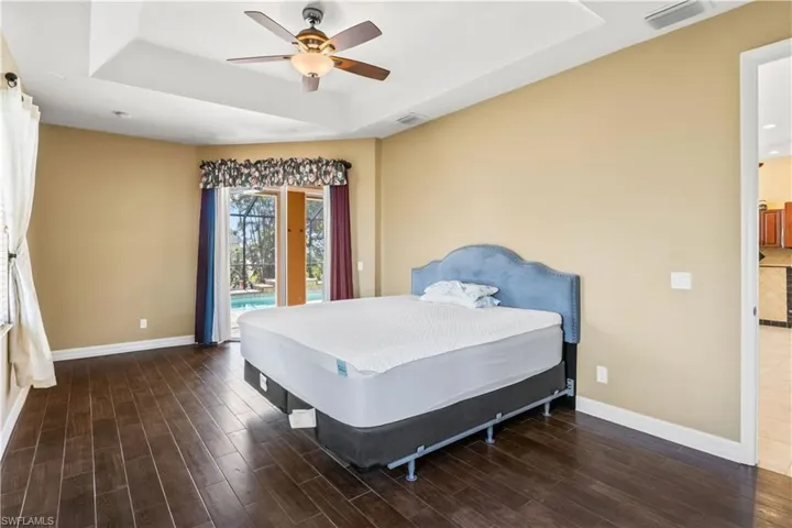Bedroom with access to exterior, dark wood-type flooring, a raised ceiling, and ceiling fan