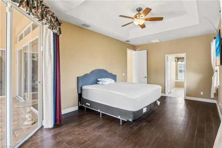 Bedroom with access to exterior, a tray ceiling, dark hardwood / wood-style floors, and ceiling fan