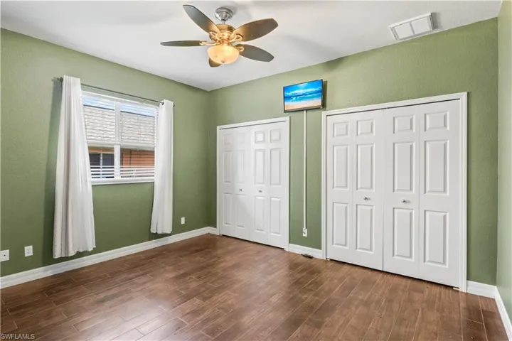 Unfurnished bedroom featuring multiple closets, ceiling fan, and dark hardwood / wood-style flooring