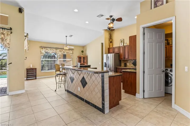 Kitchen featuring light tile patterned flooring, a breakfast bar area, decorative light fixtures, stainless steel fridge, and washer / clothes dryer