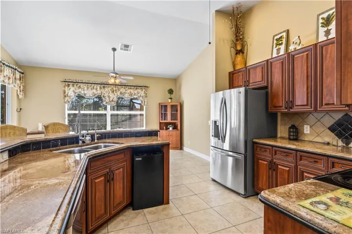 Kitchen featuring ceiling fan, backsplash, stainless steel refrigerator with ice dispenser, light tile patterned flooring, and vaulted ceiling