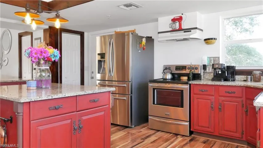 Kitchen featuring stainless steel appliances, hanging light fixtures, light wood finished floors, under cabinet range hood, and light stone counters