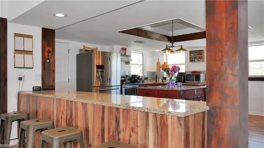 Kitchen with light stone counters, stainless steel appliances, a peninsula, a center island, and a tray ceiling