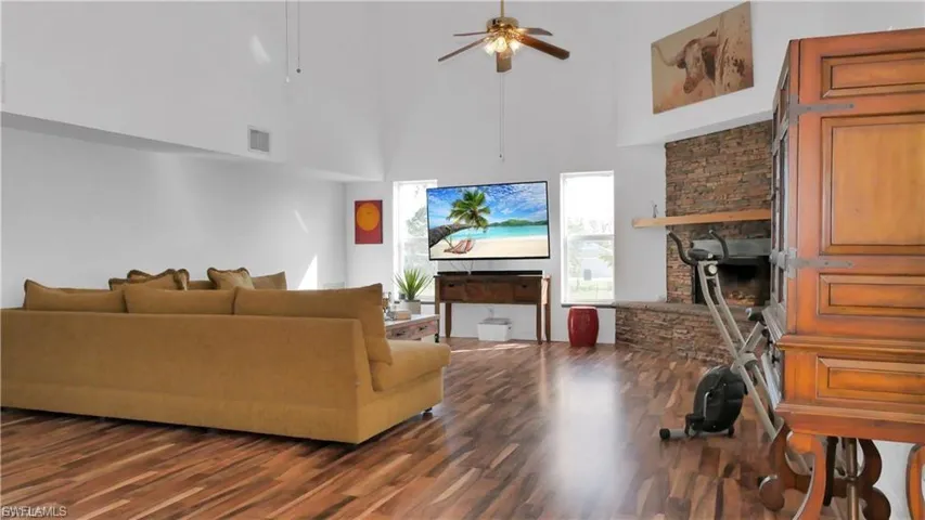Living room with a stone fireplace, a towering ceiling, dark wood-type flooring, and ceiling fan