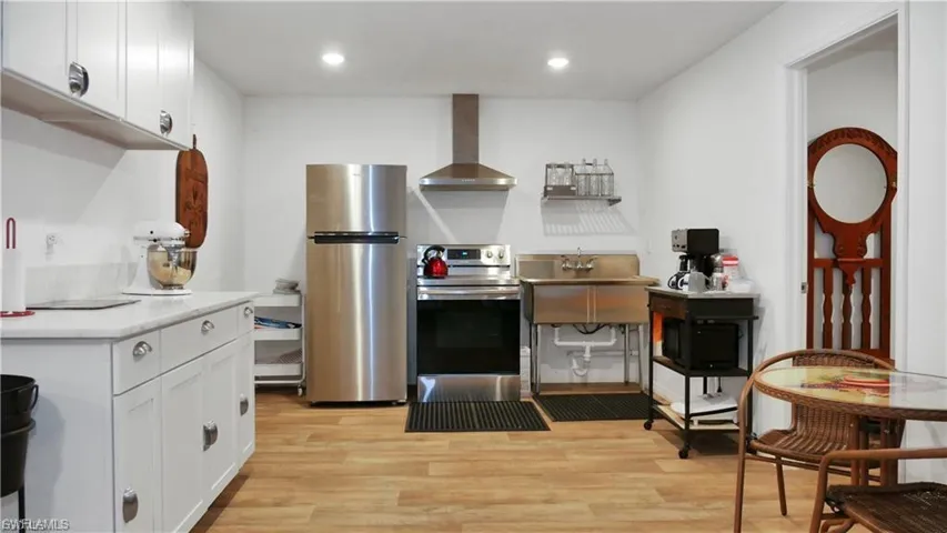 AIRBNB Kitchen with light countertops, appliances with stainless steel finishes, white cabinets, light wood-type flooring, and wall chimney range hood