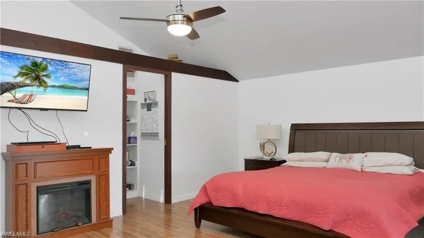 Bedroom featuring wood finished floors, a ceiling fan, vaulted ceiling, and a glass covered fireplace