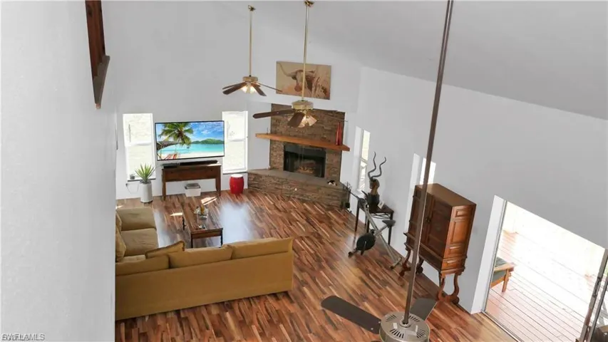 Living area with high vaulted ceiling, wood finished floors, a stone fireplace, and a ceiling fan