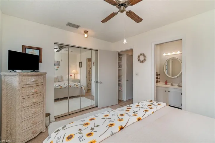 Primary bedroom featuring a closet, connected bathroom, ceiling fan, sink, and light colored carpet