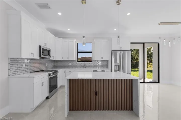 Kitchen with appliances with stainless steel finishes, decorative light fixtures, a kitchen island, and a healthy amount of sunlight