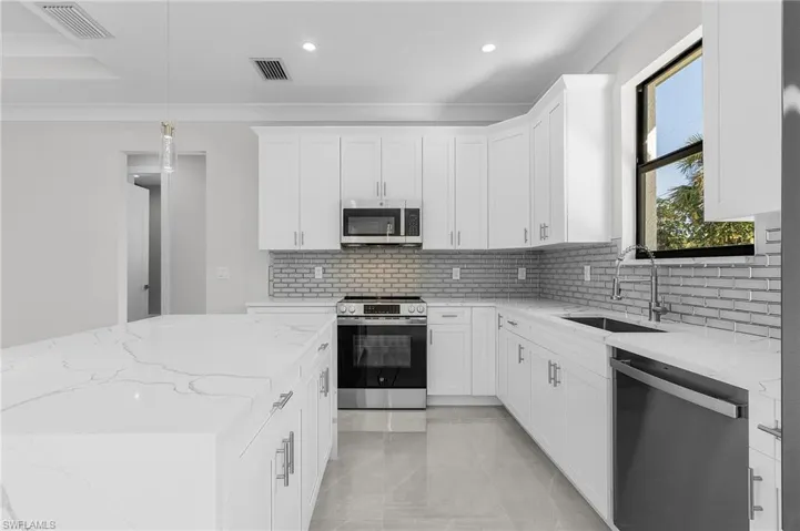 Kitchen featuring white cabinets, hanging light fixtures, sink, light stone countertops, and appliances with stainless steel finishes