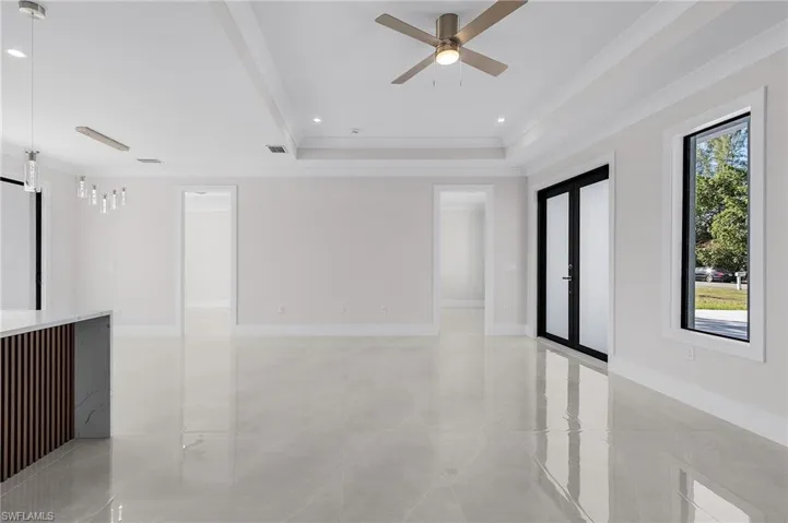 Empty room featuring a tray ceiling, crown molding, ceiling fan, and a healthy amount of sunlight