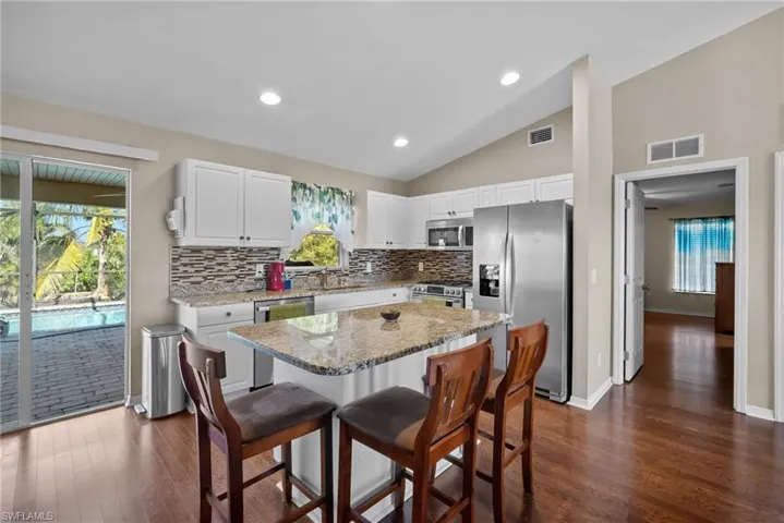 Kitchen with stainless steel appliances, light stone countertops, white cabinetry, lofted ceiling, and a kitchen breakfast bar
