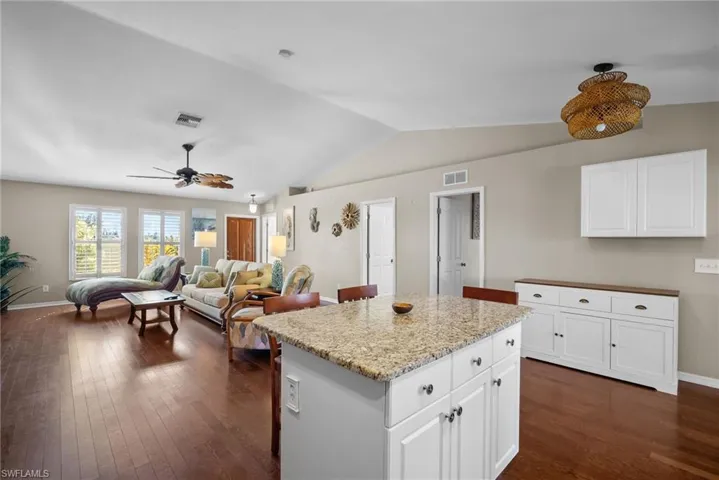 Kitchen with white cabinetry, a center island, vaulted ceiling, light stone counters, and open floor plan